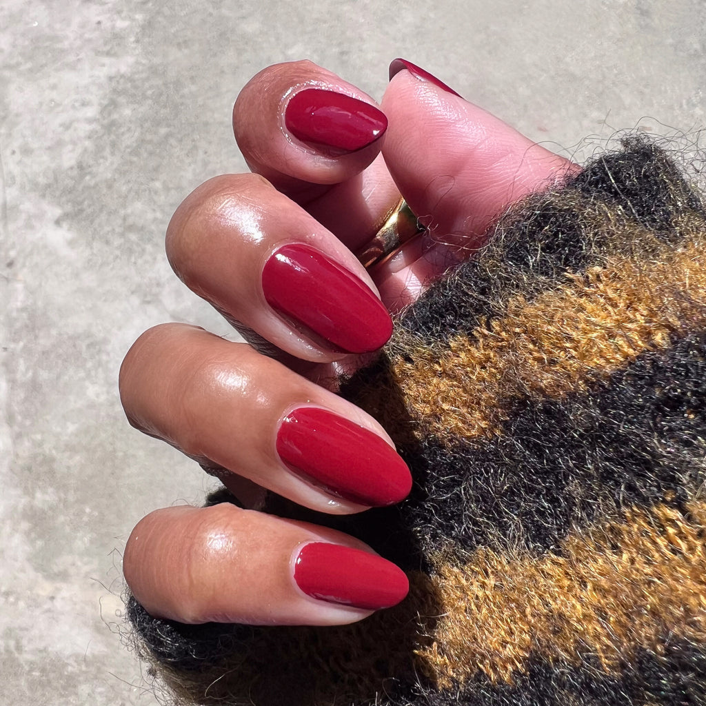 Hand with Brick polish showing rich deep red manicure on natural skin wearing a cozy striped sweater in outdoor light