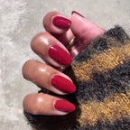 Hand with Brick polish showing rich deep red manicure on natural skin wearing a cozy striped sweater in outdoor light