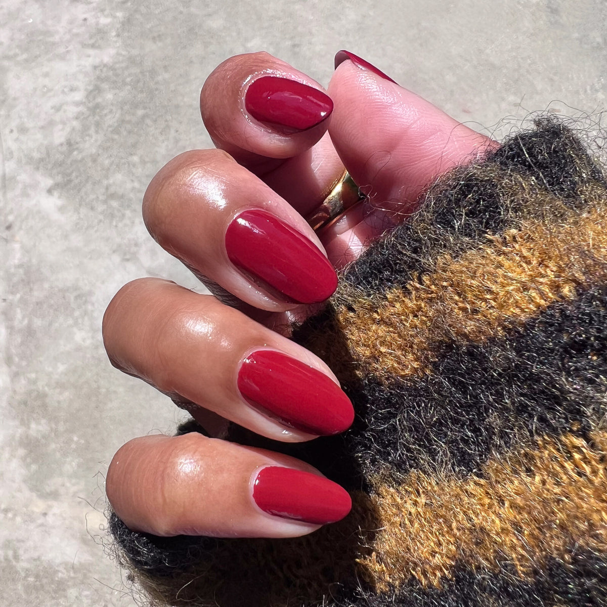 Hand with Brick polish showing rich deep red manicure on natural skin wearing a cozy striped sweater in outdoor light