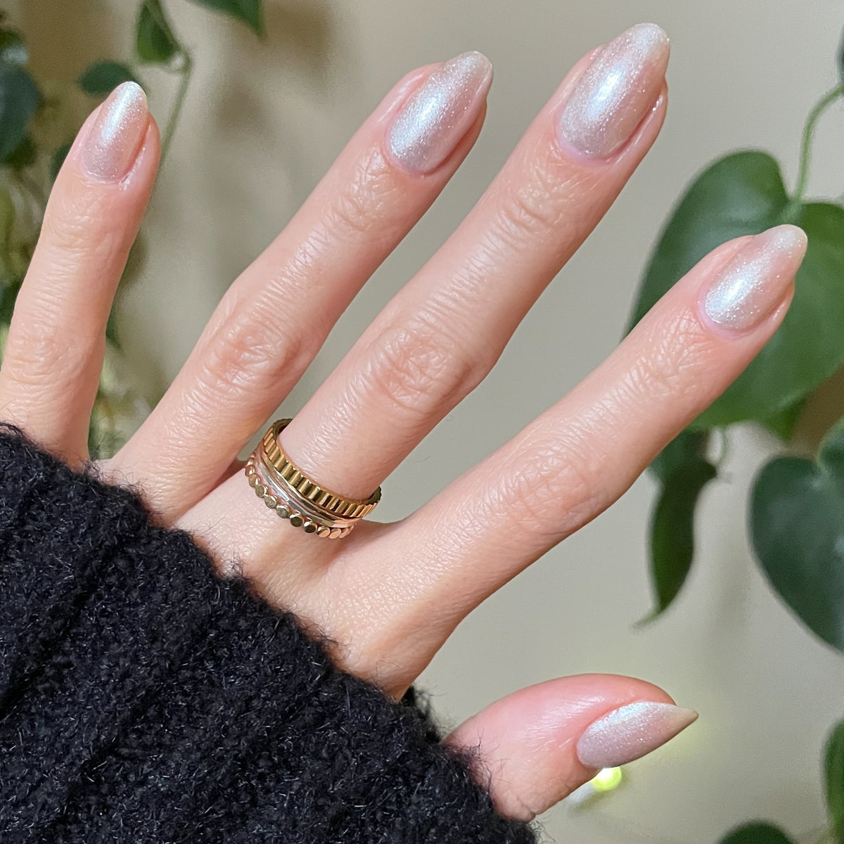 Hand with almond-shaped nails featuring subtle shimmer manicure in Midnight Disco polish against plant background