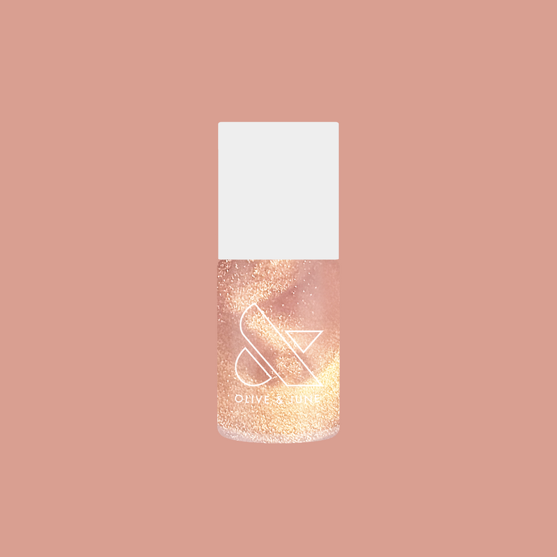 Olive and June Gold Drops nail polish bottle sparkling with gold glitter on a muted warm pink background for mani display
