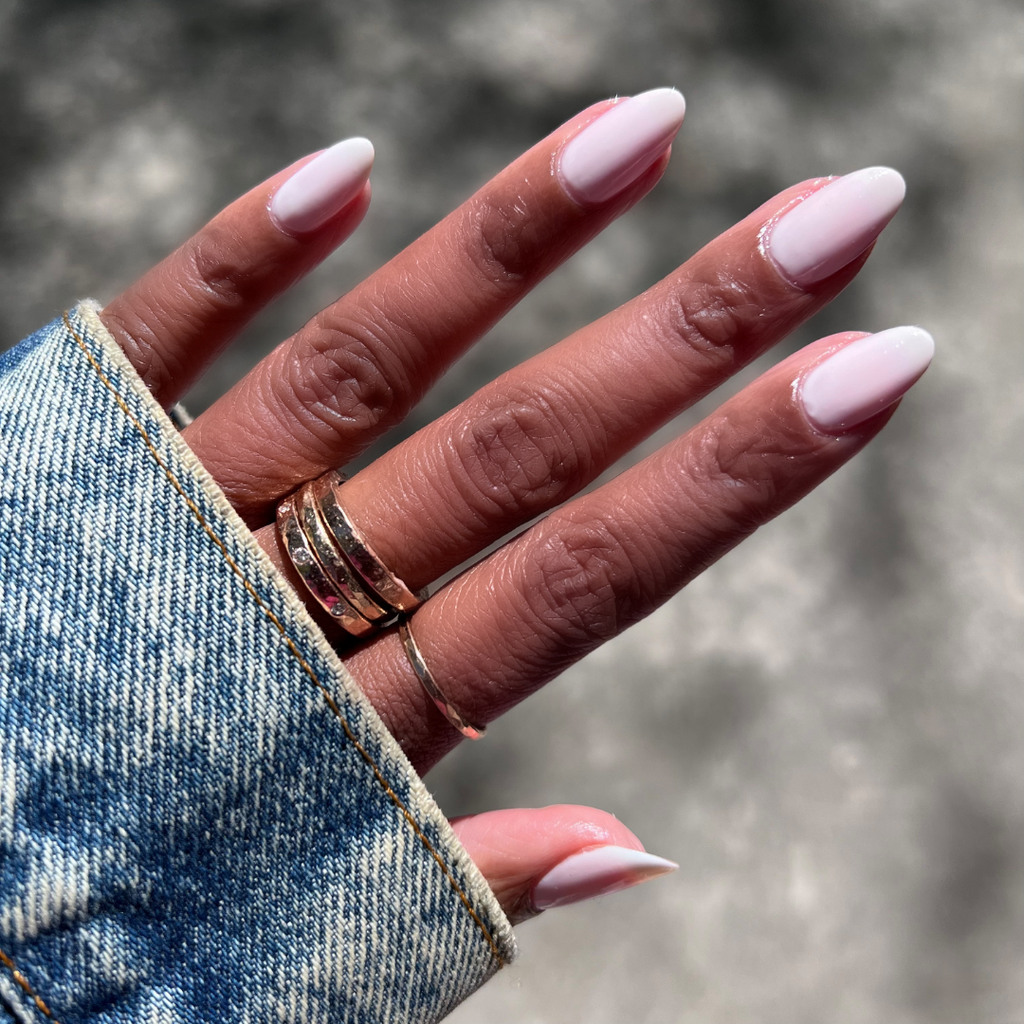 Hand with long almond nails coated in Buttercream sheer milky white polish for a smooth, frosted manicure look outdoors