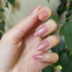 Hand with almond-shaped nails painted in Lovenote frosty pink pearl quick dry polish against blurred greenery background