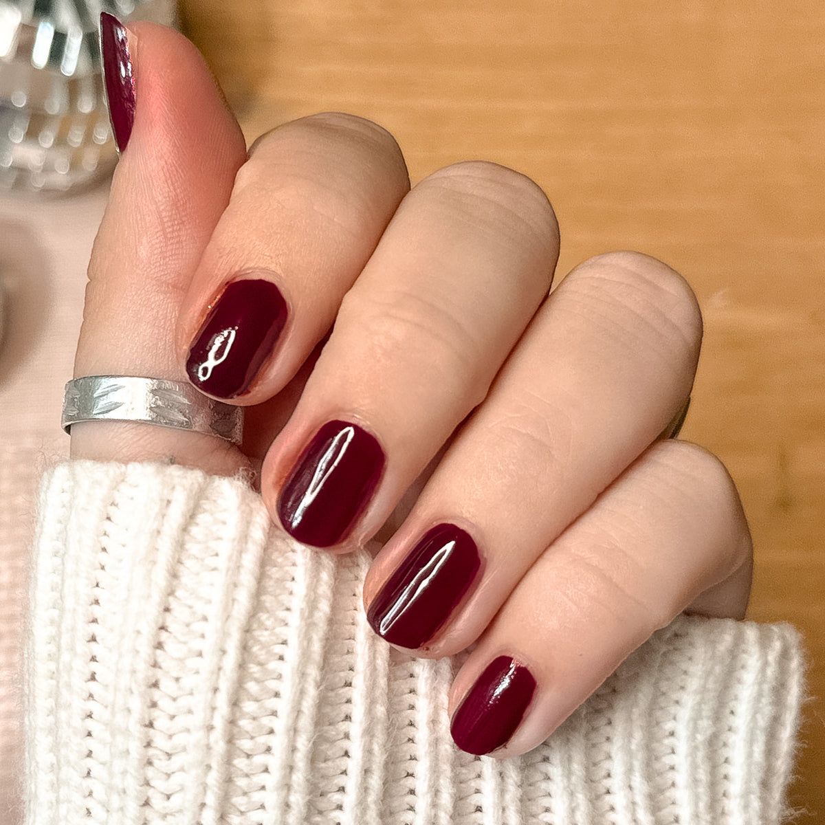 Hand with light skin tone wearing Luxe Loafer gel polish in deep crimson jelly for a shiny, long-lasting manicure indoors