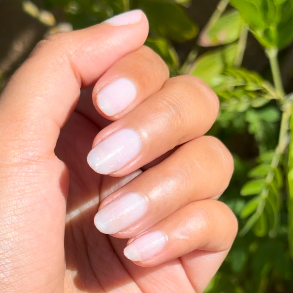 Hand with glossy milky white opal gel polish manicure using Office Party by Olive and June outdoors in natural light