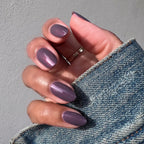 Hand with Twilight gel polish showing a smooth iridescent violet manicure in natural light against a denim sleeve
