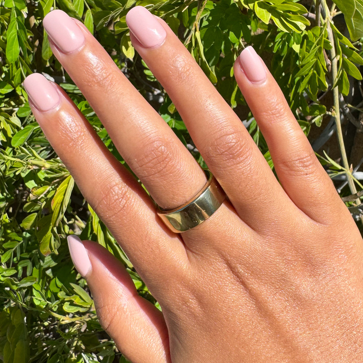 Poodle | Extra Short | Squoval - Tab Press-On nails in soft neutral beigey pink polish on hand outdoors with gold band ring