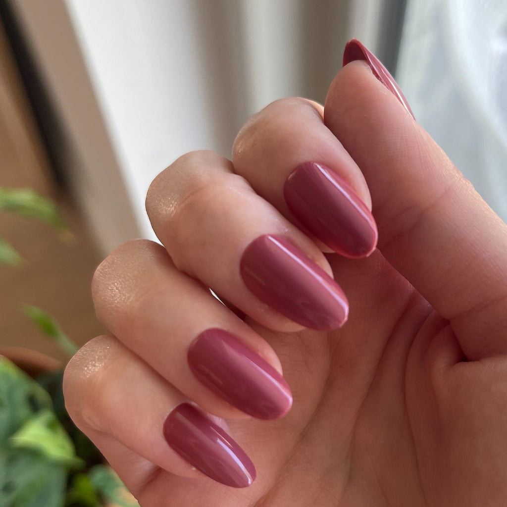 LD - Press-On | Medium | Oval showing hand with medium oval rosy mauve press-on manicure indoors near window light and plants