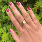 Hand with Brick polish showing smooth deep earthy red manicure on natural skin with green foliage background