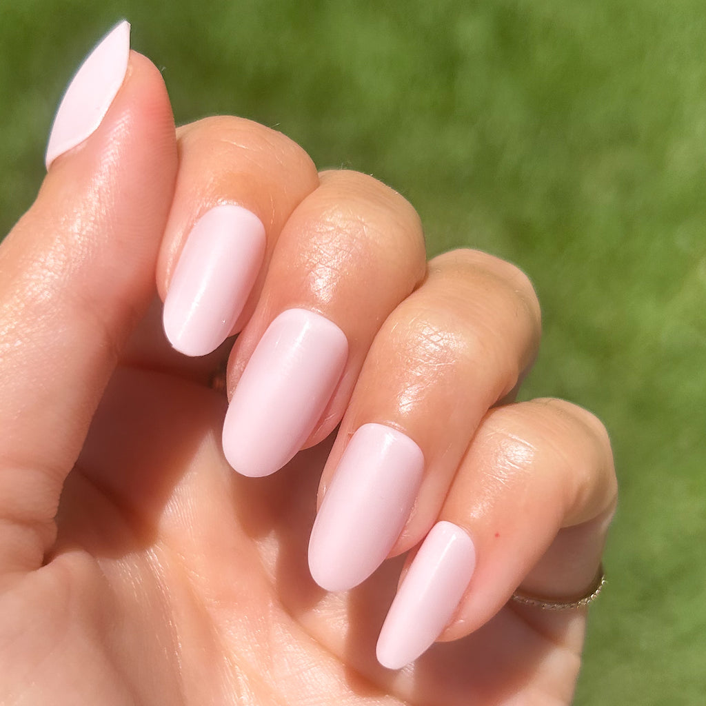 GH - Press-On | Medium | Oval showing hand with medium oval opaque glowy baby pink press-on manicure outdoors on natural green background