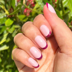 Plum Tonal French - Press-On | Short | Round showing hand with short round false nails featuring plum tips outdoors with green plants background