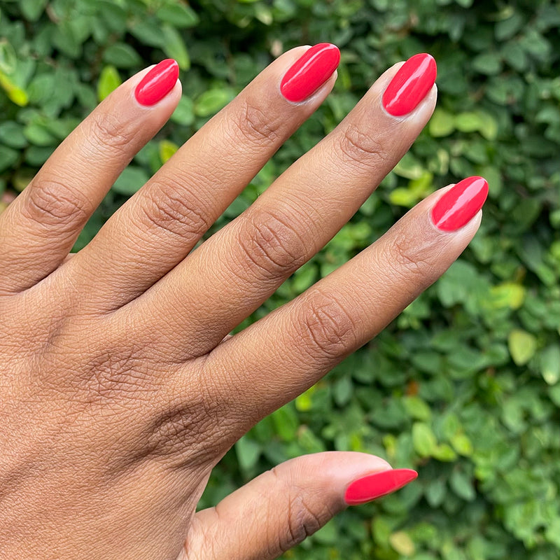 Hand with smooth red nails polished using Domino’s Pizza Mani Kit shown against green leafy background