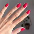 Hand with shiny red polished nails using Domino’s Pizza Mani Kit shown with blurred indoor plant background thumbnail