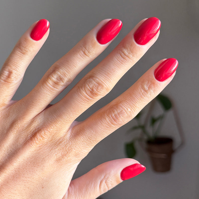 Hand with shiny red polished nails using Domino’s Pizza Mani Kit shown with blurred indoor plant background