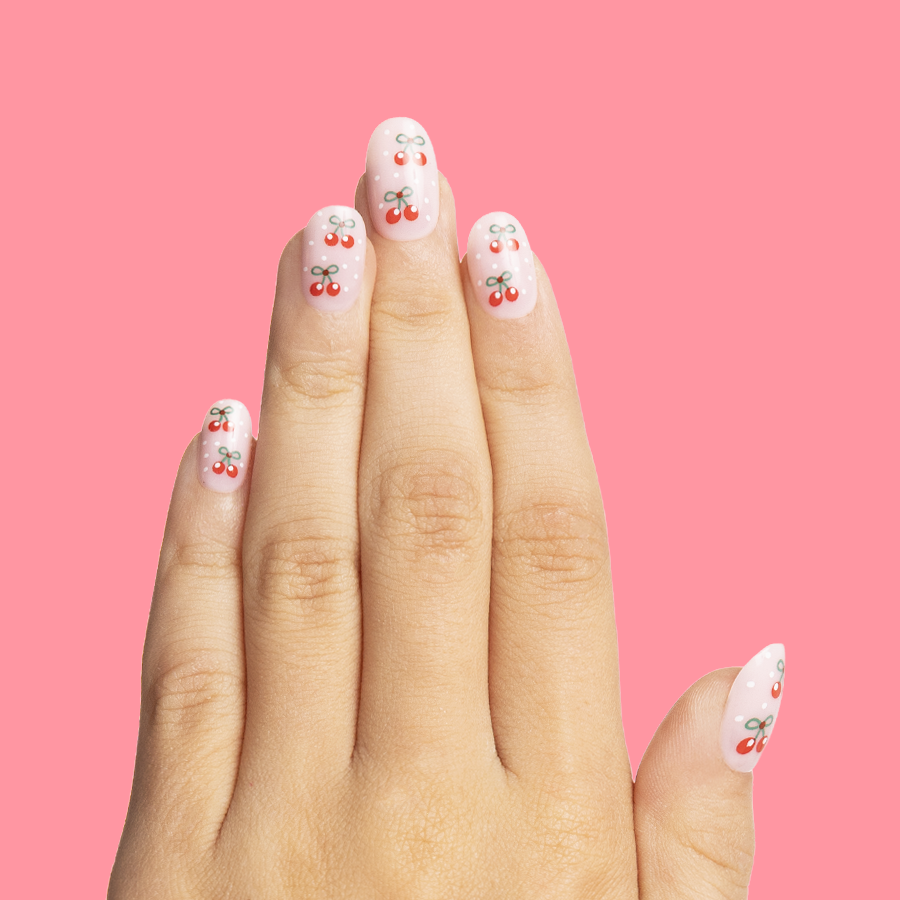 Cherry Whirl - Pressies | Short Medium | Round showing pastel pink press on nails with cherry designs on hand against pink background