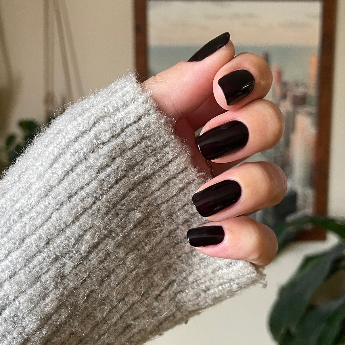 Hand with glossy Covet gel polish manicure in dark plum shade on medium-length nails wearing cozy knit sweater sleeve