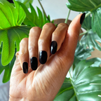 Hand with glossy Covet gel polish manicure in rich dark plum on medium-length nails against green leafy background