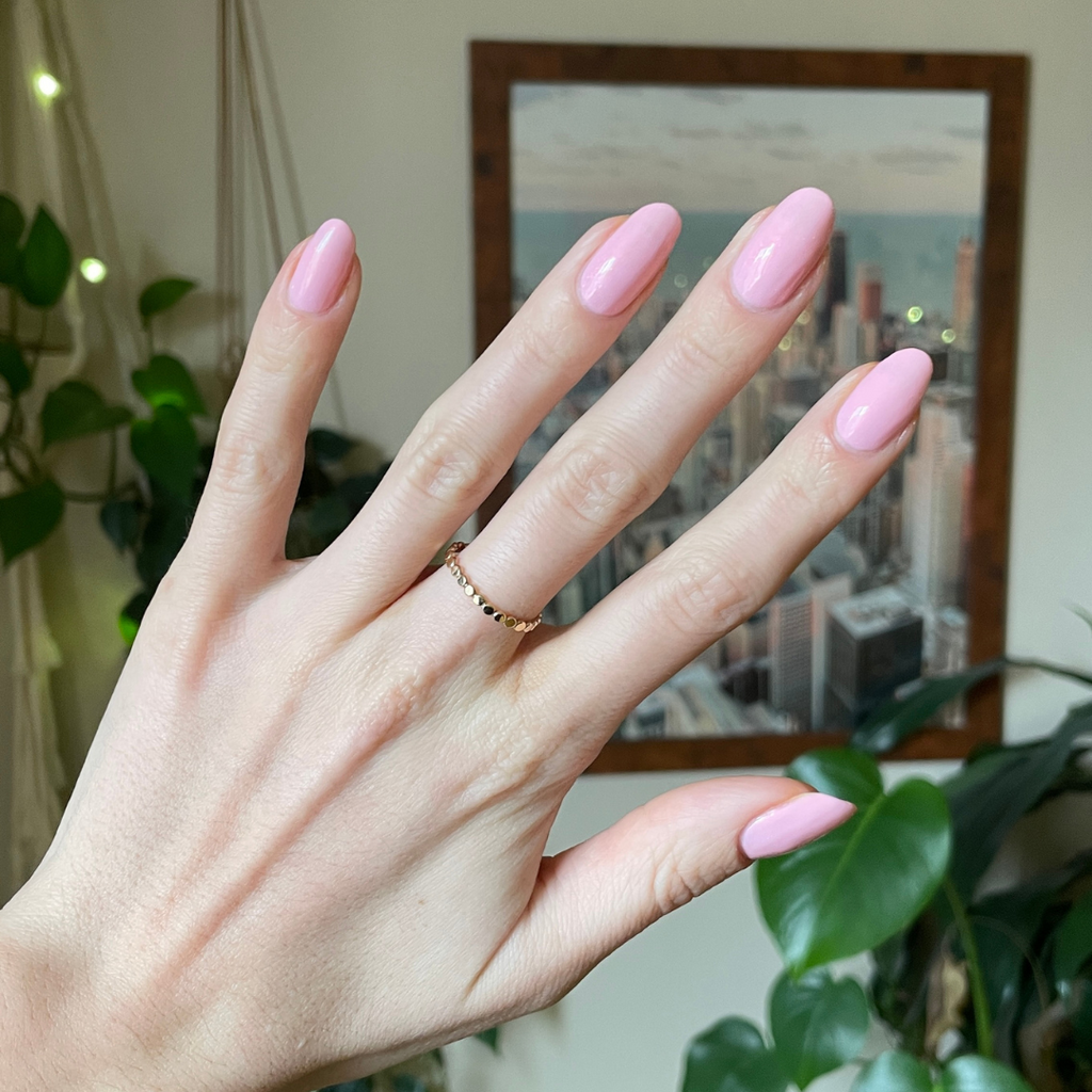 Hand with almond-shaped nails painted in Crown shimmery princess pink gel polish showing a smooth manicure indoors