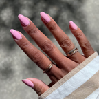 Hand with medium-length nails painted in Crown shimmery princess pink gel polish showing a glossy mani outdoors in natural light
