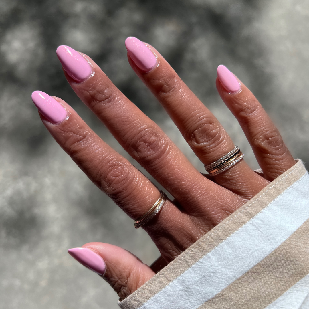 Hand with medium-length nails painted in Crown shimmery princess pink gel polish showing a glossy mani outdoors in natural light