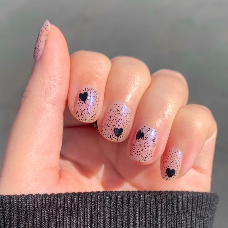 Valentine Mini Polish Set nails with sheer nude base, black speckles, and black heart accents for a subtle mani look