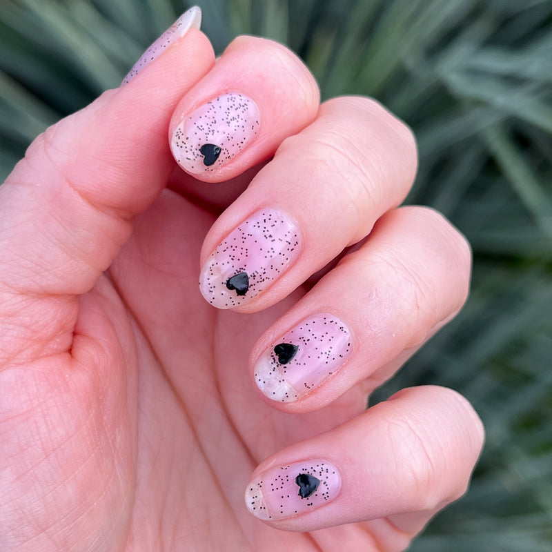 Valentine Mini Polish Set nails with sheer pink polish and black heart and tiny speckled accents for a delicate mani look