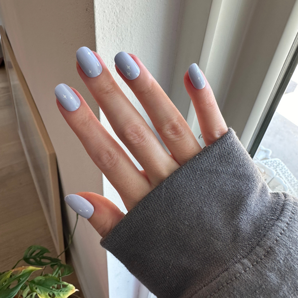 Sparkle Accent | Short | Round - Tab Press-On showing hand with light blue mani and white star sparkles near window light