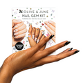 Hand with black nail polish and gold accents holding Olive and June Nail Gem Kit packaging with decorated mani examples thumbnail