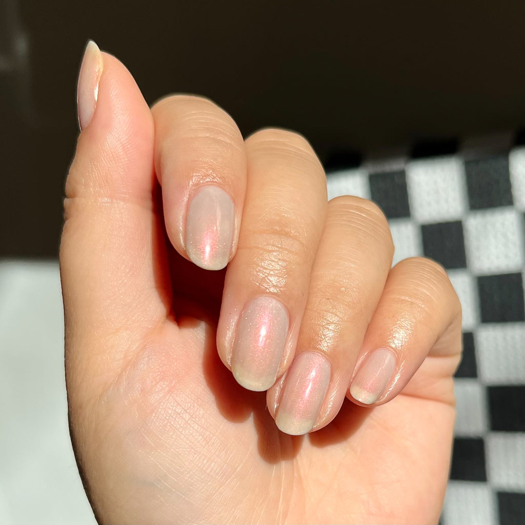 Hand with light skin tone nails painted in iridescent milky grey Elevator quick dry polish for an at home manicure