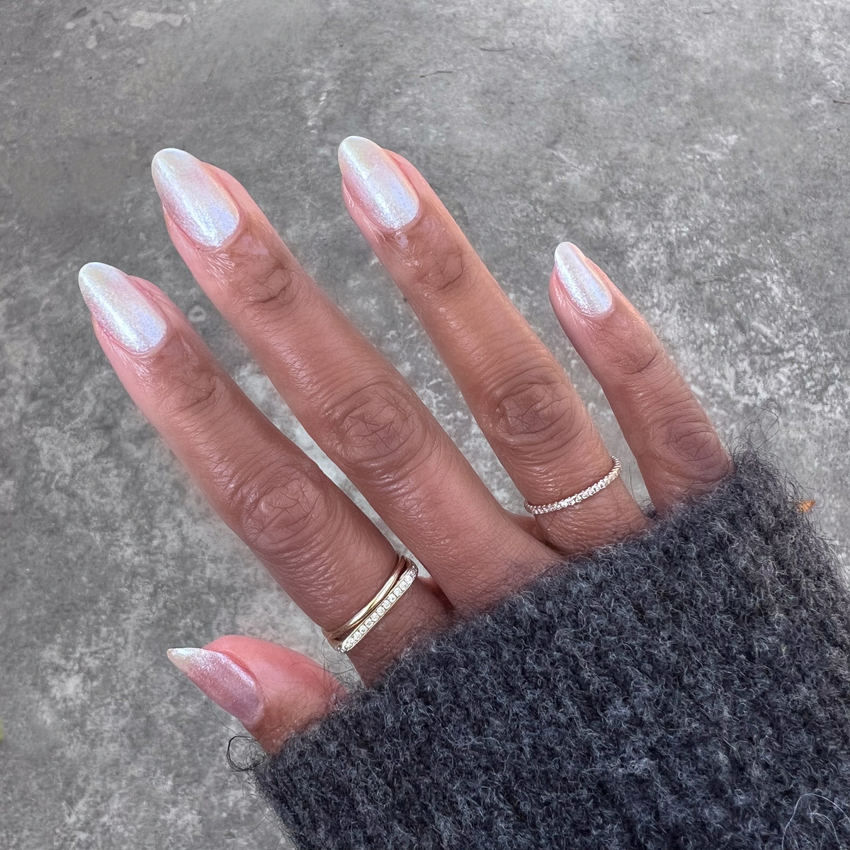 Hand with medium-length nails wearing shimmering iridescent manicure using Midnight Disco polish against stone background