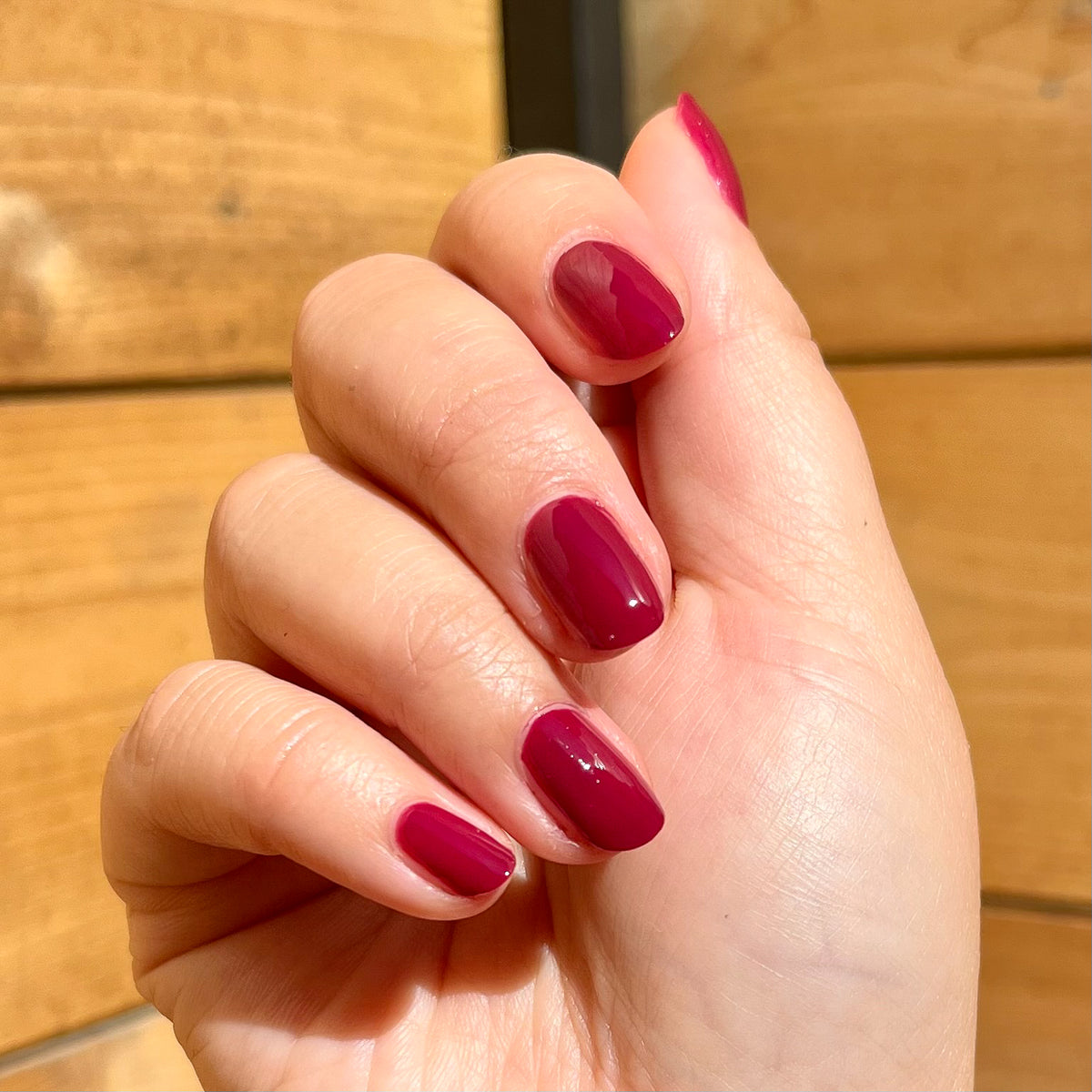 Hand with glossy Cabernet polish in deep plummy red showing a neat, rich manicure in natural sunlight at home