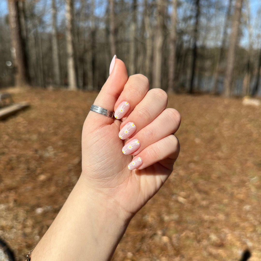Daisy Chain - Press-On | Short | Round showing short round nails with delicate white daisy designs on sheer neutral base outdoors