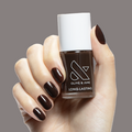 Hand with Dark Chocolate long-lasting nail polish by Olive & June on short rounded nails against neutral background
