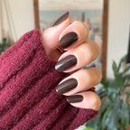 Hand with Dark Chocolate nail polish on medium-length almond-shaped nails against cozy burgundy sweater background