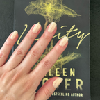 Team Manuscript - Press-On | Short | Squoval showing semi-sheer gold glazed short squoval press-on manicure on hand over book cover