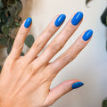 Hand showing bright blue polished nails using Domino’s Pizza Mani Kit on indoor background with plants thumbnail