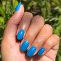 Hand with smooth blue nails polished using Domino’s Pizza Mani Kit shown against outdoor greenery background thumbnail
