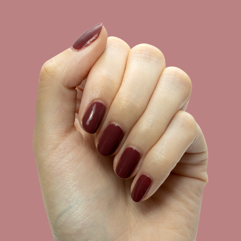 Hand with short nails painted in Don’t Spill on the White Couch deep dusty berry red gel polish manicure