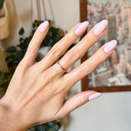 Hand with almond-shaped nails painted in FIRST DATE sheer milky strawberry pink with ultra fine silver glitter manicure