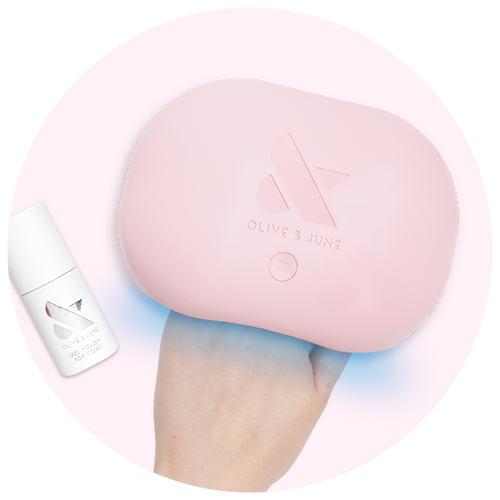Hand holding a pink Olive and June gel polish curing lamp with a matching white gel polish top coat bottle nearby
