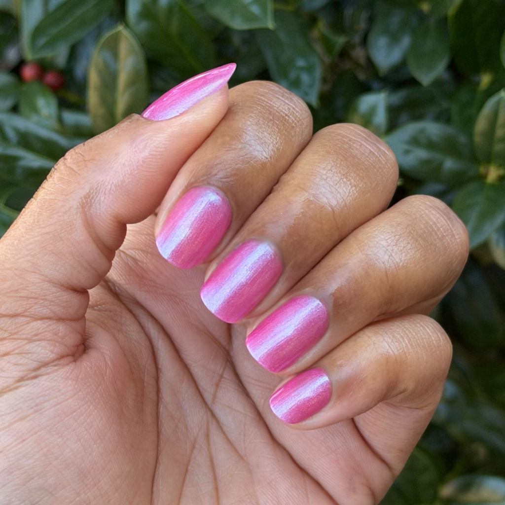 Hand with nails painted in HARD LAUNCH pinky-purple iridescent duochrome polish against natural green leaves background