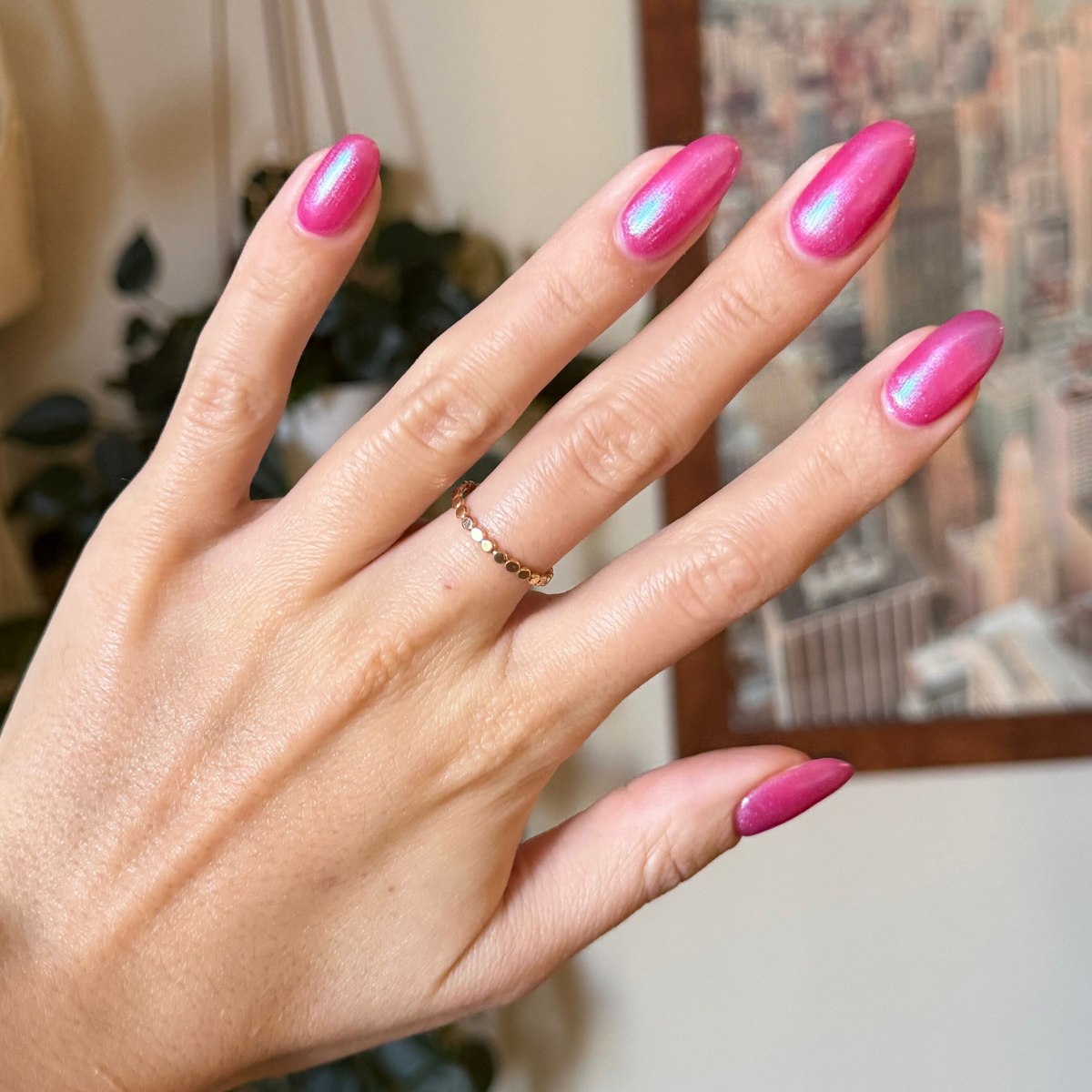 Hand with almond-shaped nails coated in HARD LAUNCH pinky-purple iridescent duochrome polish indoors background