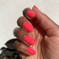 Hand with oval nails coated in bright coral-pink gel polish against a soft off-white background thumbnail