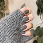 Hand with medium-length nails painted in Is it Smoky in Here? deep charcoal gray gel polish wearing cozy gray sweater sleeve