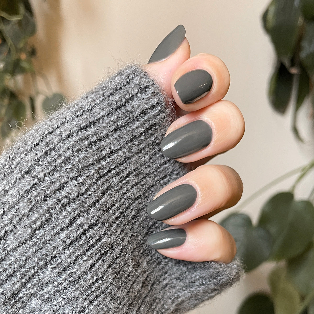 Hand with squared medium-length nails polished in Is it Smoky in Here? deep charcoal gray gel polish wearing soft gray knit sleeve