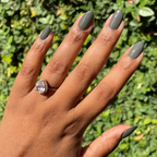 Hand with almond-shaped nails polished in Is it Smoky in Here? deep charcoal gray gel polish outdoors with sunlight
