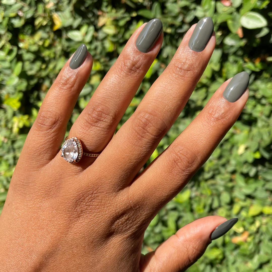 Hand with almond-shaped nails polished in Is it Smoky in Here? deep charcoal gray gel polish outdoors with sunlight