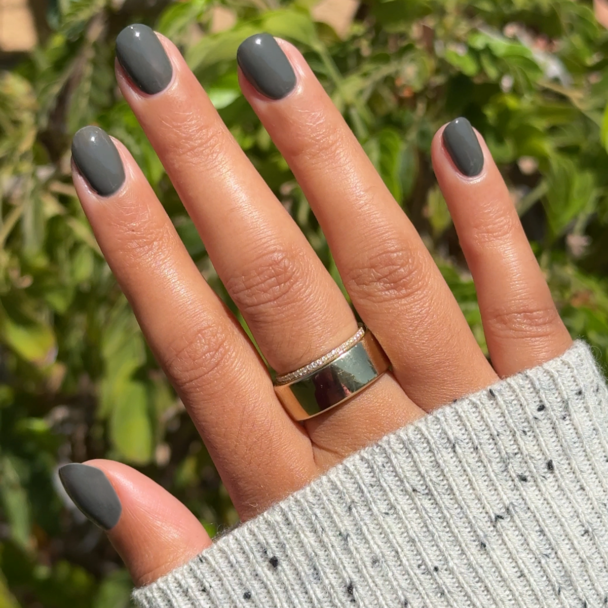 Hand with medium-length nails polished in Is it Smoky in Here? deep charcoal gray gel polish outdoors wearing light gray sweater sleeve
