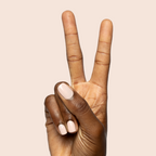 Hand showing peace sign with nails painted in KAG - Gel neutral peachy pink gel polish on light beige background