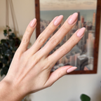 Hand with almond-shaped nails painted in KAG - Gel neutral peachy pink gel polish against blurred cityscape background